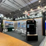 The Display+ booth at ISE 2025 in Barcelona, featuring an elegant and professional design. The booth showcases advanced display technologies with multiple screens displaying vivid visuals, including a train and underwater scenes, emphasizing the company's expertise in customized display solutions. The setup includes a spacious arrangement of white chairs and tables for discussions, along with a prominent black display stand. The branding of "ZHENGDA DSP TECHNOLOGY CO., LTD." is clearly visible, reinforcing the company's identity. The overall layout creates an inviting atmosphere, highlighting innovation and a commitment to excellence in display technology.